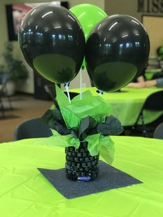 two black balloons in a vase on top of a table with green and black decorations