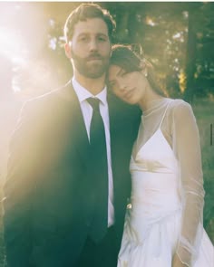 a man and woman standing next to each other in front of some trees with the sun shining on them