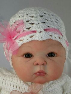 a baby wearing a white knitted hat with pink bows