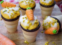 carrot cupcakes with icing and sprinkles on them are arranged in cones