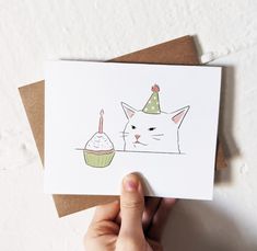 a hand holding up a card with a cat wearing a birthday hat and cupcake on it