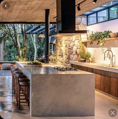 an outdoor kitchen with stone walls and flooring is featured in this image, along with bar stools that sit on the concrete countertop