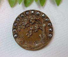 a gold brooch with an image of a bird and tree surrounded by beads on a white background