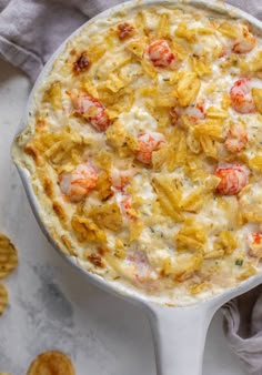 a casserole dish with shrimp and cheese in it on a table next to crackers