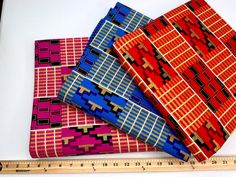 three pieces of cloth are next to a ruler on a white surface with red, blue and yellow designs