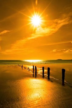 the sun is setting over the beach with some poles sticking out of the ocean water