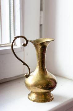 a gold vase sitting on top of a white window sill next to a window