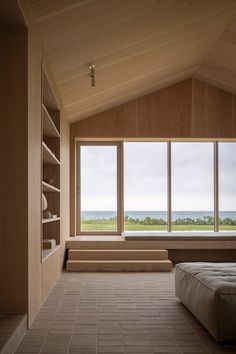 an empty room with large windows and a bed in the corner, along with bookshelves