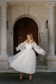 a woman in a white dress is standing on the steps outside an old building with columns