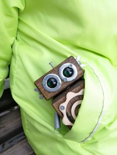 an old camera is in the pocket of someone's green parka, which also has eyeballs on it