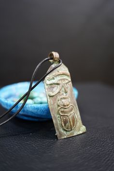 a necklace with a face on it sitting in front of a blue bowl and black background