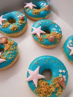 six donuts decorated with blue icing and starfish on display in a box