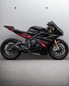 a black and red motorcycle parked in front of a gray wall on concrete flooring