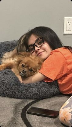 a woman laying on top of a bed with a dog in her lap and smiling at the camera