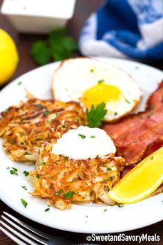 a white plate topped with eggs, hash browns and lemon wedges next to a fork