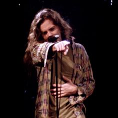 a man with long hair holding a microphone in his right hand while standing on stage