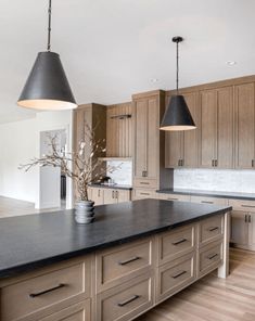 a large kitchen with wooden cabinets and black counter tops, two pendant lights over the island