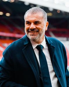 a man wearing a suit and tie standing in front of an empty stadium stands smiling