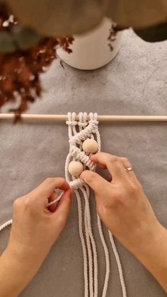 a woman is working on something with white yarn and wood bead balls in her hands