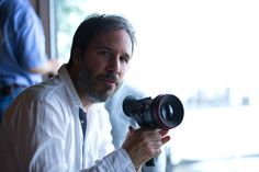 a man holding a camera in his right hand and looking at the camera with an intense look on his face