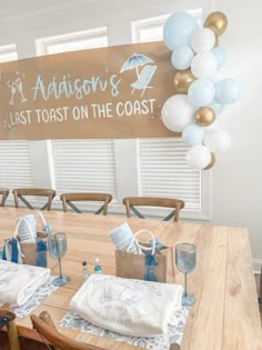 a wooden table topped with lots of white and blue balloons next to a sign that says madison's last toast on the coast