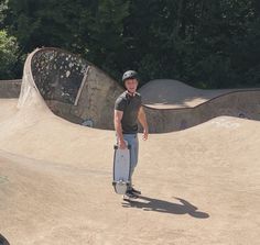 a man standing on top of a skateboard ramp at a skate park with trees in the background