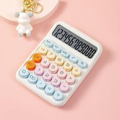 a white calculator sitting on top of a pink table next to a keychain