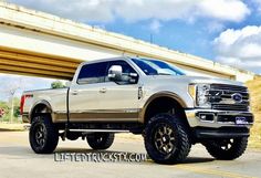 a white truck parked in front of a highway under an overpass with the words lifted trucks on it