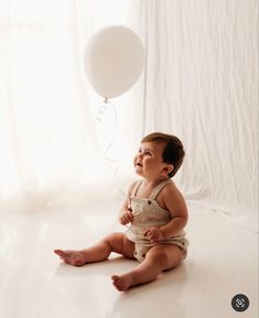 a baby sitting on the floor with a balloon in front of him and looking up