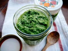 two jars filled with green pesto sitting on top of a table next to spoons