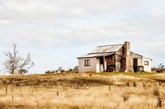 an old house sits in the middle of a field with dry grass and tall grasses