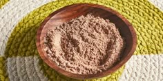 a wooden bowl filled with brown powder on top of a yellow and white rug next to a wood spoon