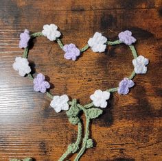 a crocheted heart with flowers and leaves attached to it on a wooden surface