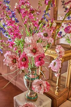 a vase filled with pink and purple flowers on top of a table next to a mirror