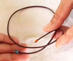 two hands are holding a brown cord that is connected to an orange and blue bead