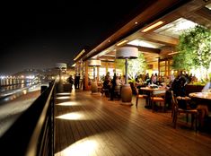 people are sitting at tables on a deck overlooking the water