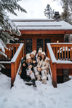 group of people sitting on steps in front of cabin with snow covered ground and pine trees