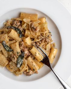 a white plate topped with pasta and meat covered in sauce next to a silver fork