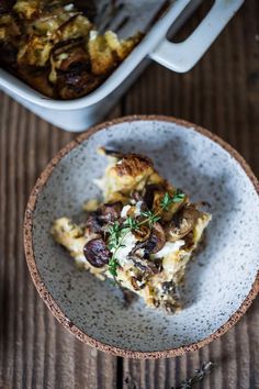 a white bowl filled with food next to a casserole dish on top of a wooden table