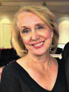 an older woman with blonde hair smiling at the camera while standing next to a man in a suit