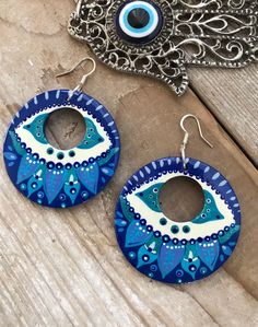 two blue and white circular earrings sitting on top of a wooden table next to an eye