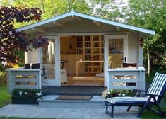 a small white shed sitting on top of a grass covered field next to a lawn chair