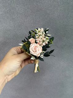 a hand holding a bouquet of flowers on top of a gray surface with white and pink flowers