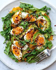 a white plate topped with an egg and avocado salad next to a fork