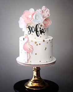 a three tiered cake with pink and white flowers on top, sitting on a gold pedestal