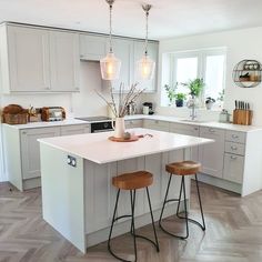 a kitchen with two stools in front of an island and white cabinets, surrounded by wood flooring