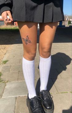 a person in a skirt and white socks with tattoos on their legs is standing on the sidewalk