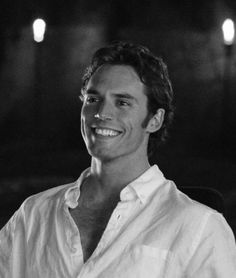 a black and white photo of a man in a shirt smiling at the camera with lights behind him