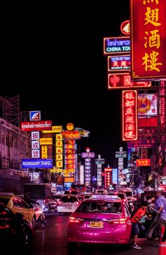 a busy city street at night with neon signs and cars driving on the road in front of it