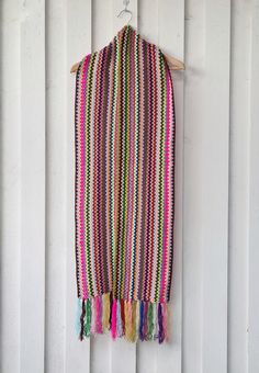 a multicolored scarf hanging on a white wall with wood slats in the background